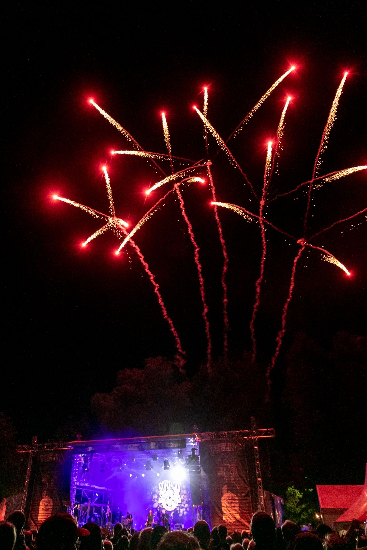Rotes Feuerwerk steigt über der violett beleuchteten Festivalbühne in den Nachthimmel