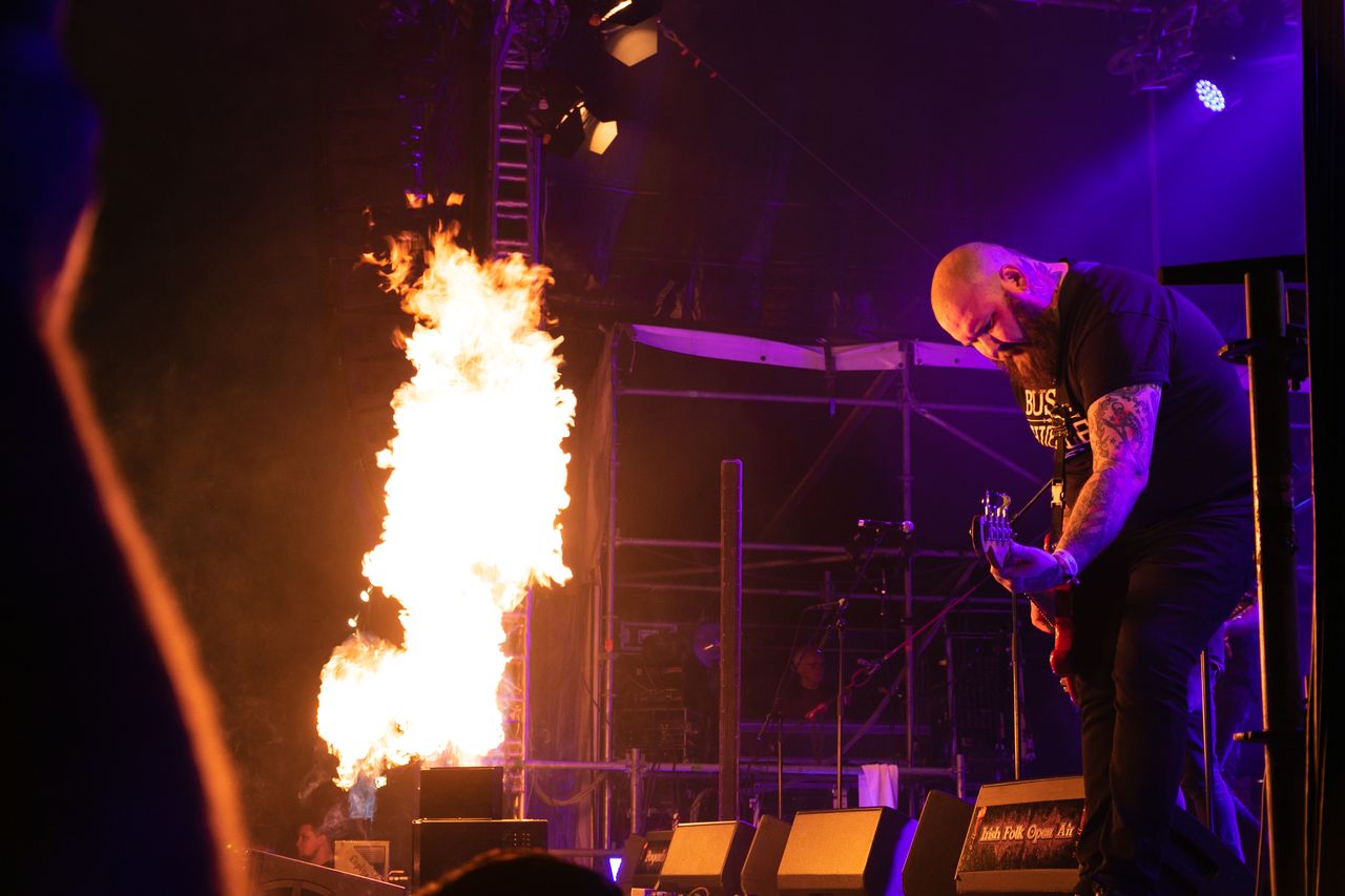 Flammensäule auf der Bühne, daneben spielt der Bassist von The Rumjacks im violetten Licht