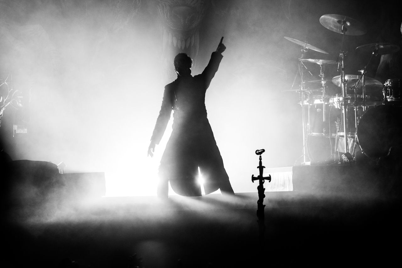 Schwarz-weiße Silhouette des Powerwolf-Sängers mit erhobenem Arm vor grellem Gegenlicht und Bühnennebel