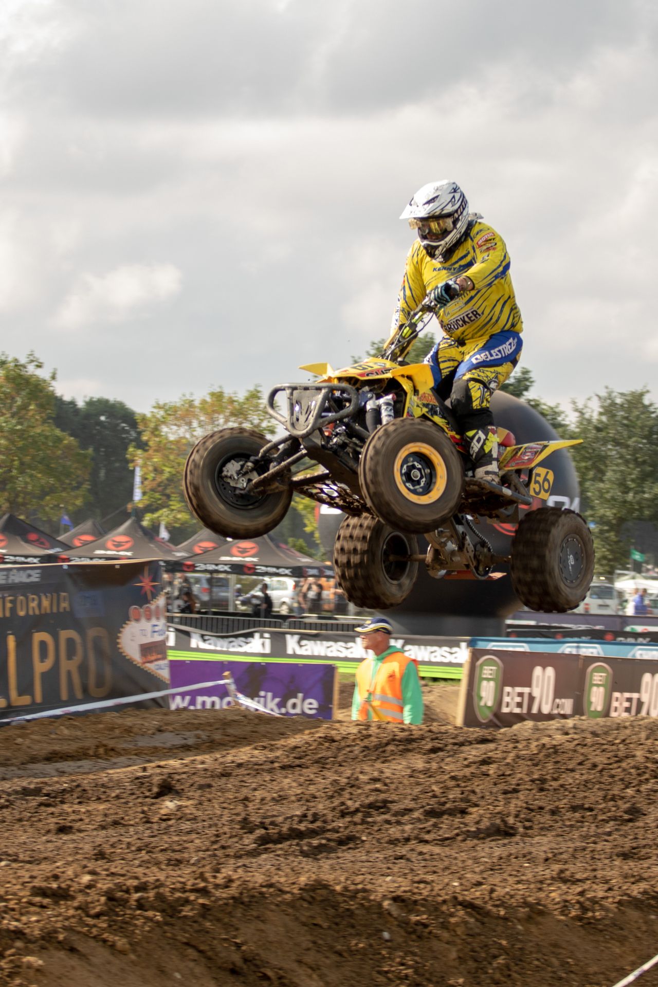 Quad-Fahrer in gelber Montur hebt beim Sprung über die Motocross-Strecke ab