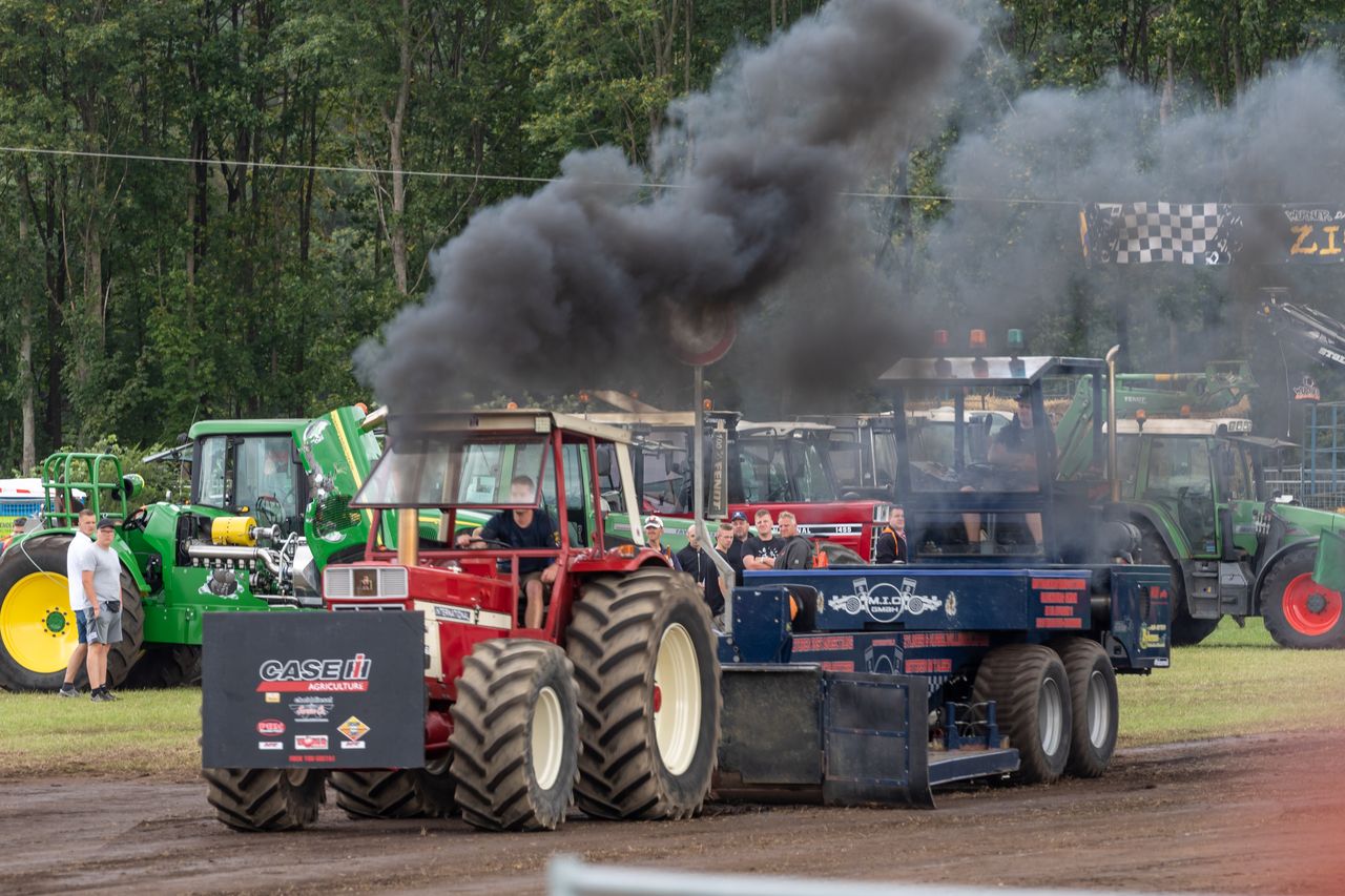Roter Traktor zieht beim Tractor Pulling den Bremsschlitten und stößt eine schwarze Rauchwolke aus